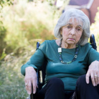 Depressed Senior Woman In Wheelchair Sitting Outdoors