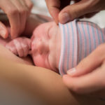 New born boy on mom's chest. Dad adjusting hat.