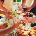 Human hands with glasses of red wine clinking them over served table.