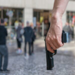 Armed man (attacker) holds pistol in public place. Many people on street. Gun control concept.