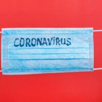 Female hands in medical gloves holding protective mask with coronavirus text on it at red background. Health care concept. Coronavirus concept