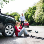 Young woman by the car after an accident and a man running towards her.