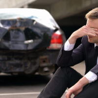 Desperate man sitting asphalt on crashed car background, automobile accident